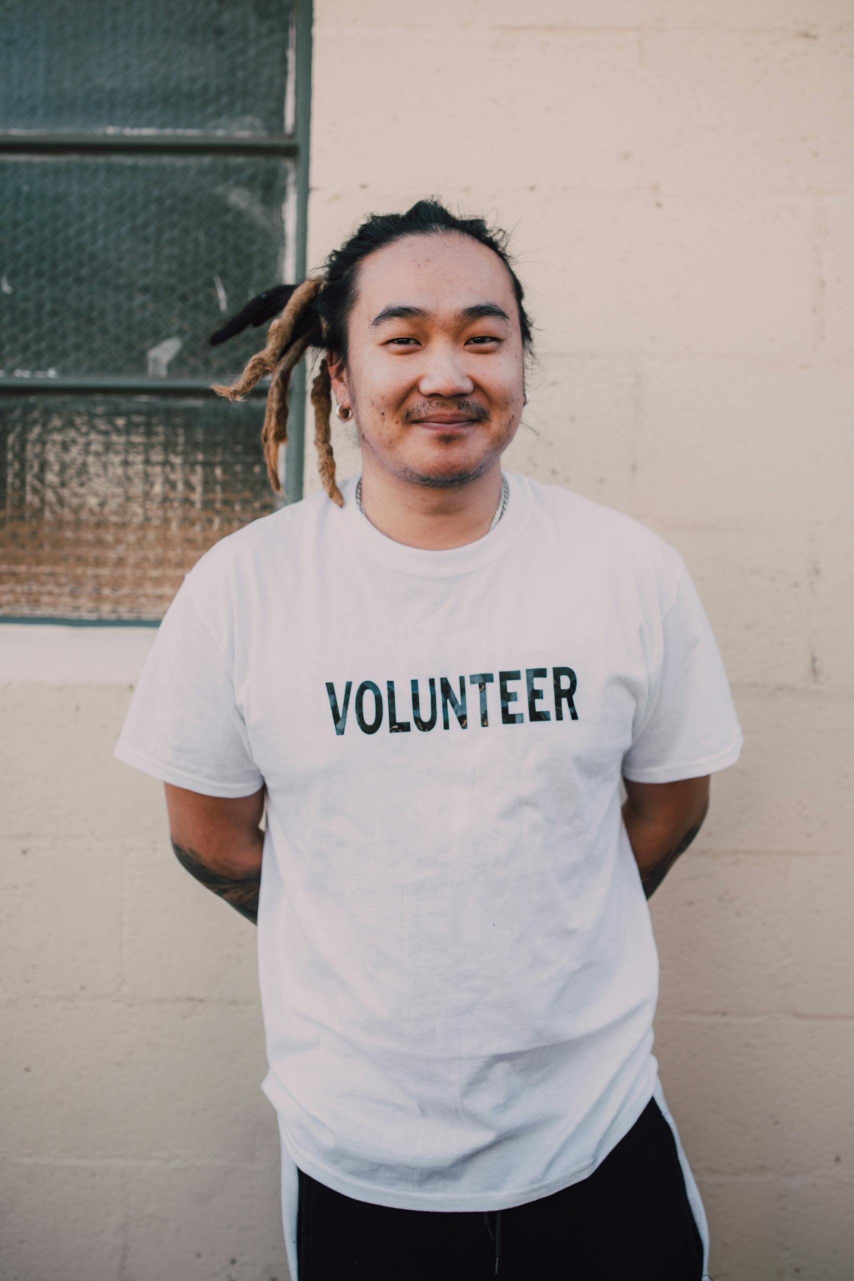 Portrait of a young male volunteer with dreadlocks standing outdoors, embodying community spirit and social good.